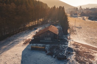 Wooden house on the edge of the forest, surrounded by snow, captured in the warm light of sunset