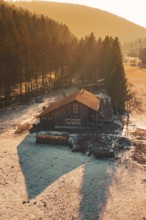 Wooden house on the edge of a forest whose shadows are cast in the snow by warm sunset light,