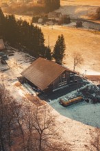 Snowy wooden house in a rural area, illuminated by the warm light tones of sunset, Enzklösterle,