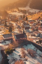 Snowy village with central church, warm sunlight bathes the surrounding area in golden tones,