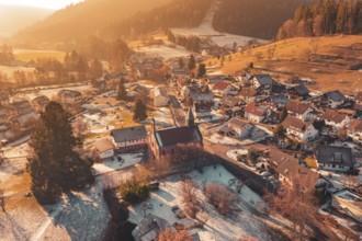 Snowy village with central church surrounded by snow-covered houses and warm golden light,