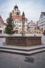 A fountain on a market square surrounded by historic buildings and a distinctive church tower under