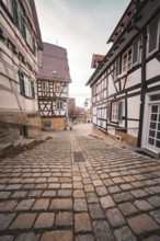 Narrow paved alley lined with charming half-timbered houses under overcast sky, Herrenberg,