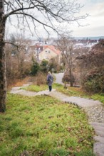 A woman walks down a stone staircase surrounded by trees and autumn leaves in an urban park,