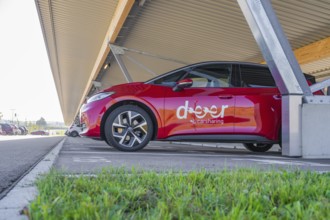Red car sharing car under covered parking lot in sunny weather. Modern urban environment, ID3, Deer