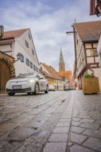 Electric car drives through a cobblestone old town with church tower, ID3, deer e-car sharing,