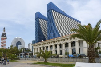 Blue skyscrapers with innovative design stand in an urban setting with palm trees and busy streets,