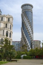 A modernly designed high-rise building with spiral balconies rises above the surrounding green