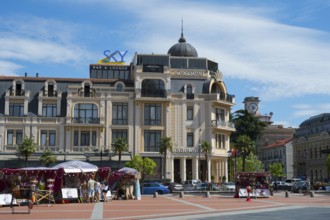 Market with stalls and people in front of a historic building with decorative roof, Royal Casino