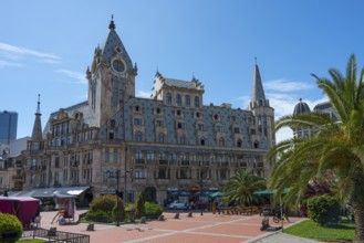 Historic building with towers and palm trees on an open square under a blue sky, Europe Square,