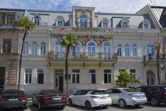 Historic building with palm trees and cars in front of it, colorful decoration over the windows,