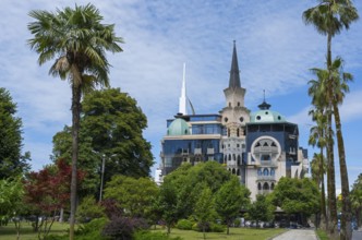Historic building with tower in the park surrounded by palm trees under a blue sky, former registry