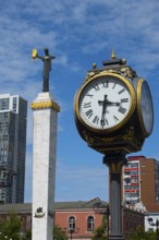 Large clock and statue in front of modern buildings under bright blue sky, clock and statue of