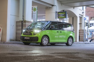 Green VW shuttle at a bus stop, modern urban atmosphere, Deer E-Mobility Shuttle Service, Calw,