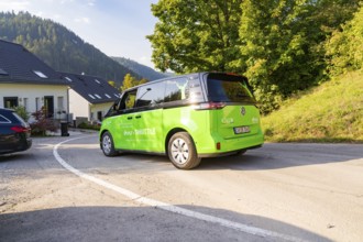 Green car on road in residential area with surrounding natural backdrop, Deer E-Mobility Shuttle