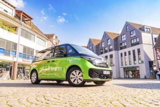 Green car in an urban square with blue sky in the background, Deer E-Mobility Shuttle Service,