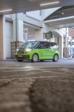 Green shuttle goes around a bend in an urban area, busy atmosphere, Deer E-Mobility Shuttle