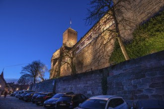 Nuremberg Kaiserburg in evening lighting, blue evening sky, cars parked below on the castle wall,