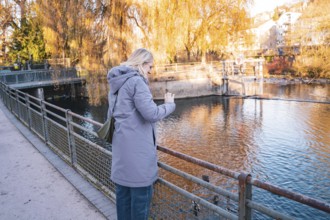 Woman photographing a river on an autumn day, Stadtgarten Pforzheim, Germany