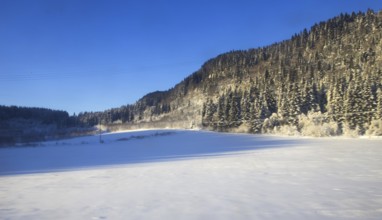 Snowy winter landscape with trees, mountains under clear blue sky Norway