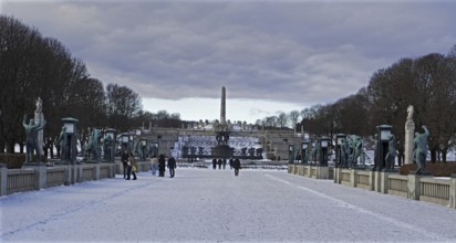 Snowy park (Vigeland Sculpture Park) with sculptures and walkers under a cloudy sky, Oslo Norway