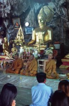Buddha statue, monks and believers praying, Wat Tam Sua monastery near Krabi, Thailand, December