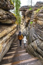 Mother and child walking down wooden stairs among layered sandstone cliffs at athabasca falls in