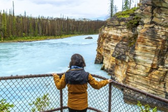 Tourist in a yellow jacket enjoying the breathtaking view of athabasca falls, surrounded by