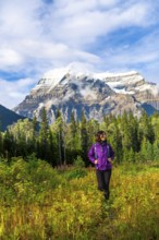 Female hiker walking through a meadow enjoying the view of mount robson on a sunny day with clouds