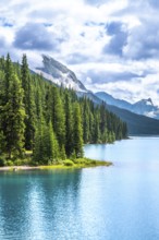 Turquoise maligne lake reflecting a cloudy sky, surrounded by lush pine forests and rocky mountains