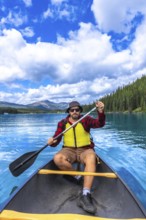 Tourist wearing sunglasses and a life jacket paddling a canoe on turquoise maligne lake under a