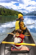Mother and son paddling a canoe on maligne lake's turquoise waters, surrounded by mountains and