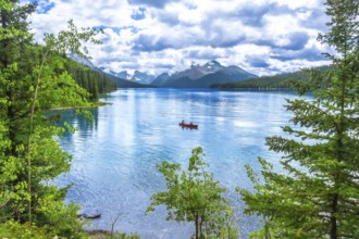 Two tourists enjoying a canoe ride on the turquoise waters of maligne lake, surrounded by lush