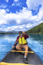 Tourist wearing sunglasses and life jacket paddling a canoe on beautiful maligne lake in jasper