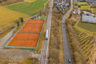 Aerial view of a landscape with railway tracks, tennis courts and roads, surrounded by fields and