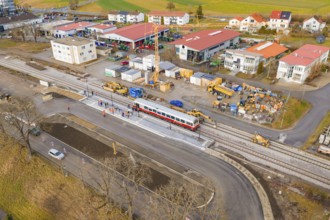 Workers and machines are working on an extensive construction site near tracks and a passing train,