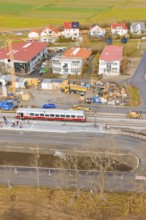 A train passes a construction site with numerous buildings and a crane in a rural area, historic