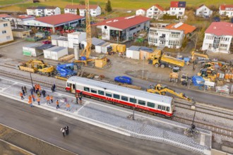 Workers work next to a train and tracks at a construction site with adjacent buildings, historic