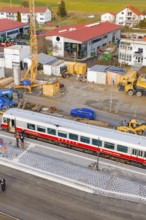 A train on a platform in the middle of a construction site with construction site vehicles and