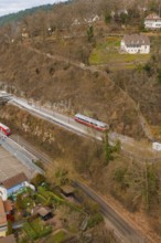 Train travels through hilly terrain with buildings and trees in a winter environment, historic