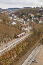 A train passes by a mountain range. In the background is a small town with many houses, historic