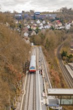 A train stops at a station on a hill with a view of a town with many buildings, historic event,