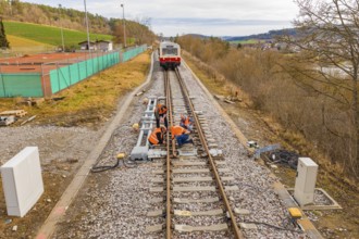 Construction workers working on railroad tracks with a train standing in the background, historic