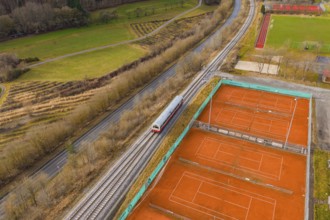 A train travels through rural surroundings next to several tennis courts and fields, historic