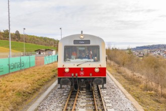 Train with passengers and the inscription 'Calw' on the rails, with landscape in the background,