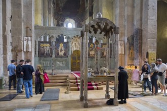 People in a traditional church interior near an altar with icon portraits, Svetitskhoveli