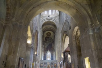 Church interior with high arches and a fresco depicting saints on a background of stone walls,
