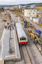 Train stops at a construction site surrounded by workers with industrial buildings in the
