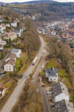 Railway line through a rural town with residential buildings on hilly, wooded terrain, historic