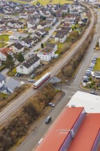 Train crossing a road junction in a residential and industrial area with red roofs, historic event,